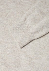Manche de pull en laine beige avec poignet côtelé, montrant une texture tricotée fine et douce.