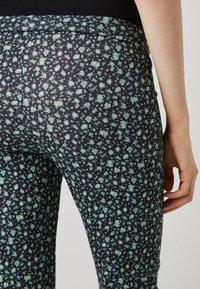 Sorte svarte leggins med et lite blomstermønster i myntegrønn. Designet med elastisk midje og glatt tekstur.