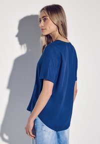 Top corto blu reale a maniche corte con scollatura rotonda, texture morbida e orlo curvo, abbinato a jeans di denim blu chiaro.