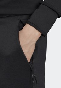 Svart tröjfabrics med en sidoficka prydd med dragkedja. Nära bild av en hand som vilar i fickan, som visar den släta texturen och design detaljer.