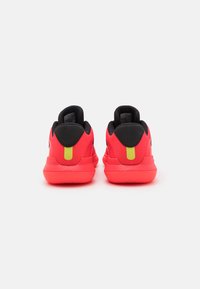 Pantofi sport roșii cu un material superior texturat, accente negre, guler căptușit și un tab de călcâi galben, având o talpă din cauciuc profilată.