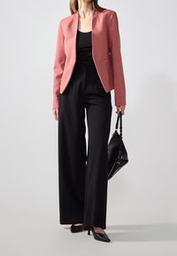 Blazer rose clair ajusté au design épuré, associé à un pantalon large noir. Des chaussures à talons noires et un sac à main noir complètent la tenue.