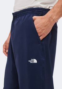 Homme portant un short bleu marine The North Face avec une ceinture élastique et une main dans la poche sur un fond uni.