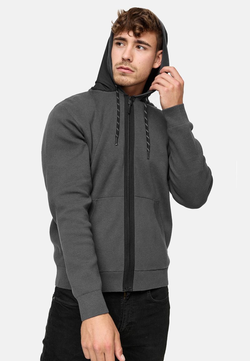 Haut à zip gris avec des accents noirs, capuche réglable avec cordon de serrage, poignets côtelés et poches, fabriqué dans un tissu doux et texturé.