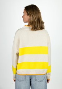 Cremfarbener Pullover mit gelben Streifen und orangefarbener gerippter Kragen, mit lockerer Passform und strukturiertem Strick. Getragen mit hochgeschnittenen Jeans.