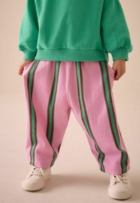 Roheline pusa soonikkoes äärega, millele on lisatud roosad püksid punase ja rohelise vertikaalse triibuga ning küljetaskutega, kantud valgete tossudega.