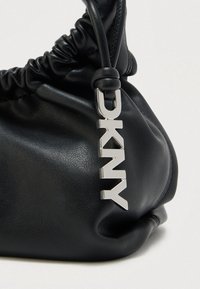 Musta nahkainen olkalaukku keräytyneellä tekstuurilla, jossa hopeinen DKNY-logo riipus kiinnitetty hihnaan. Sileä viimeistely, pehmeä muoto.