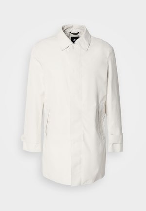 Bela, srednje dolga bunda z gumbnim zapiranjem, ovratnikom v obliki konice in dvema stranskima žepoma. Narejena iz gladkega, lahkega materiala z zavitimi manšetami.