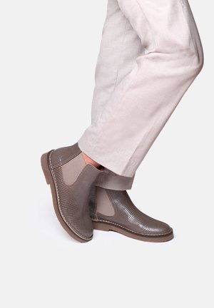 Bottines en cuir marron à motif reptile texturé et panneaux latéraux élastiques, associées à un pantalon en lin de couleur claire.