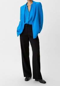 Blazer blu sopra una camicia blu, abbinato a pantaloni neri larghi e scarpe nere. Tessuto morbido con una vestibilità su misura e una silhouette strutturata.
