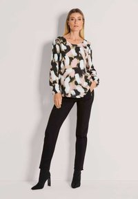 Lange mouwen top met een kleurrijk penseelstreekpatroon in zwart, wit, perzik en roze, gecombineerd met strakke zwarte broeken en laarzen met hak.