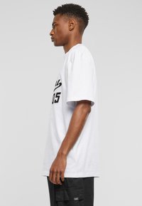Hvit bomulls t-skjorte med svart grafisk trykk på forsiden. Korte ermer og avslappet passform. Brukt med sorte cargo-shorts.