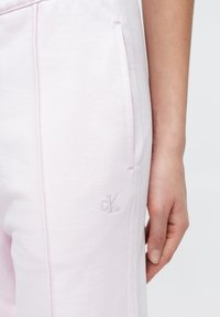 Ροζ ανοιχτό χρώμα φόρμες με υφή, με πλαϊνές τσέπες και διακριτικό κεντημένο λογότυπο "ck" κοντά στο τελείωμα.