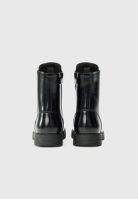 Stivali alla caviglia in pelle verniciata nera con pannelli elasticizzati, suole in gomma testurizzata e logo impresso sul tallone. Finitura liscia, design elegante.