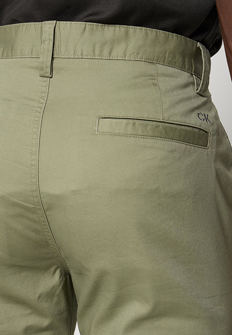 Lichtgroene katoenen broek met een gladde textuur, voorzien van een enkele achterzak en een subtiele "CK" logo-accent nabij de tailleband.