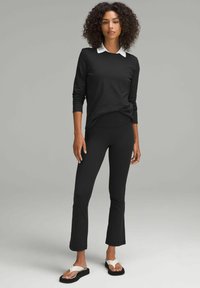 Maglietta nera a maniche lunghe con colletto bianco abbinata a leggins neri attillati e sandali bassi con cinturino bianco. Texture morbide, vestibilità casual.