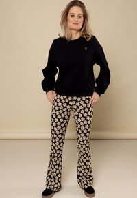 Zwarte sweatshirt met ronde hals, gecombineerd met flared broeken met een zwarte achtergrond en een crèmekleurig bloemenpatroon. Zwarte schoenen inbegrepen.