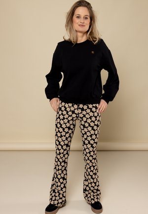 Zwarte sweatshirt met ronde hals, gecombineerd met flared broeken met een zwarte achtergrond en een crèmekleurig bloemenpatroon. Zwarte schoenen inbegrepen.