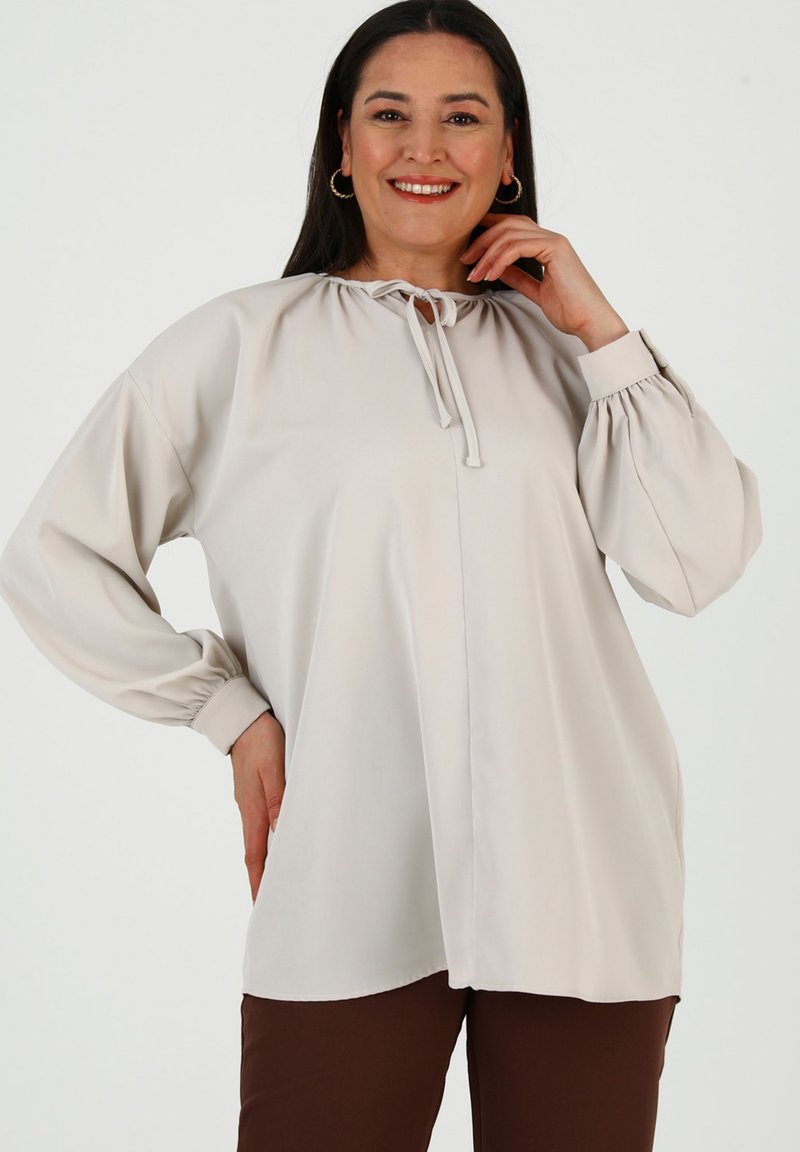 Blusa beige chiaro con scollatura rotonda e dettaglio con fiocco, caratterizzata da maniche lunghe voluminose con polsini arricciati. Tessuto morbido e vestibilità comoda.