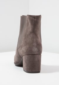 Bottine en daim marron avec un talon bloc, des panneaux latéraux élastiques et une finition lisse. Le design présente un bout arrondi et un tissu texturé.