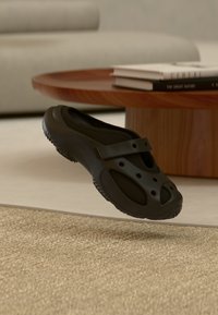 Chaussure noire  à enfiler avec dessus en maille, semelle en caoutchouc et sangle ajustable. Dotée de trous de ventilation et d'un design profilé pour le confort.