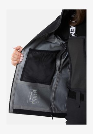 Innenansicht einer schwarzen wasserdichten Jacke mit silbernem Futter, Netzfach und Pflegeetikett, das die Stoffeigenschaften und Merkmale beschreibt.