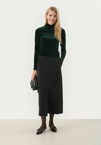 Grön sammetsturtleneck, svart knä-lång kjol med slits fram, svart handväska och spetsiga svarta ballerinas. Släta texturer och åtsittande former.