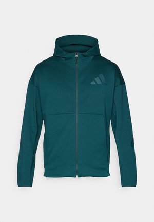 Teal mikina s kapucí na plný zip s předními kapsami a jemným tmavým logem na hrudi a rukávech, vystavená na čistém bílém pozadí.