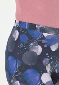 Leggings multicolori con uno sfondo scuro e motivi circolari blu e grigi, realizzati in tessuto elastico con vita elasticizzata.