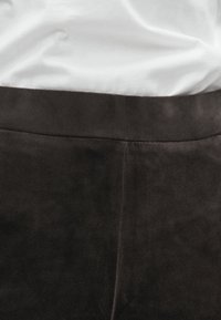 Black suede trousers feature a smooth texture and a fitted waistline, with subtle stitching along the seams and a straight leg design.