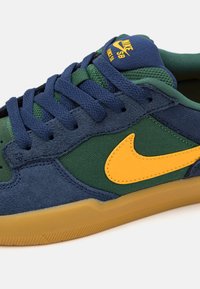 Sneakers Nike SB Force 58 z niebieskiego zamszu, zielonymi panelami z siateczki, żółtym logo Nike, granatowymi sznurówkami i gumową podeszwą.