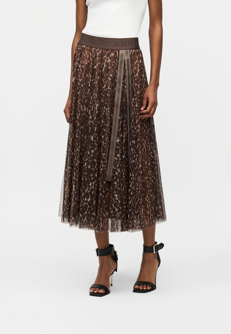 Femme portant une jupe midi à imprimé léopard marron avec une superposition en tulle, une large ceinture et des sandales à talons noirs avec brides à la cheville.