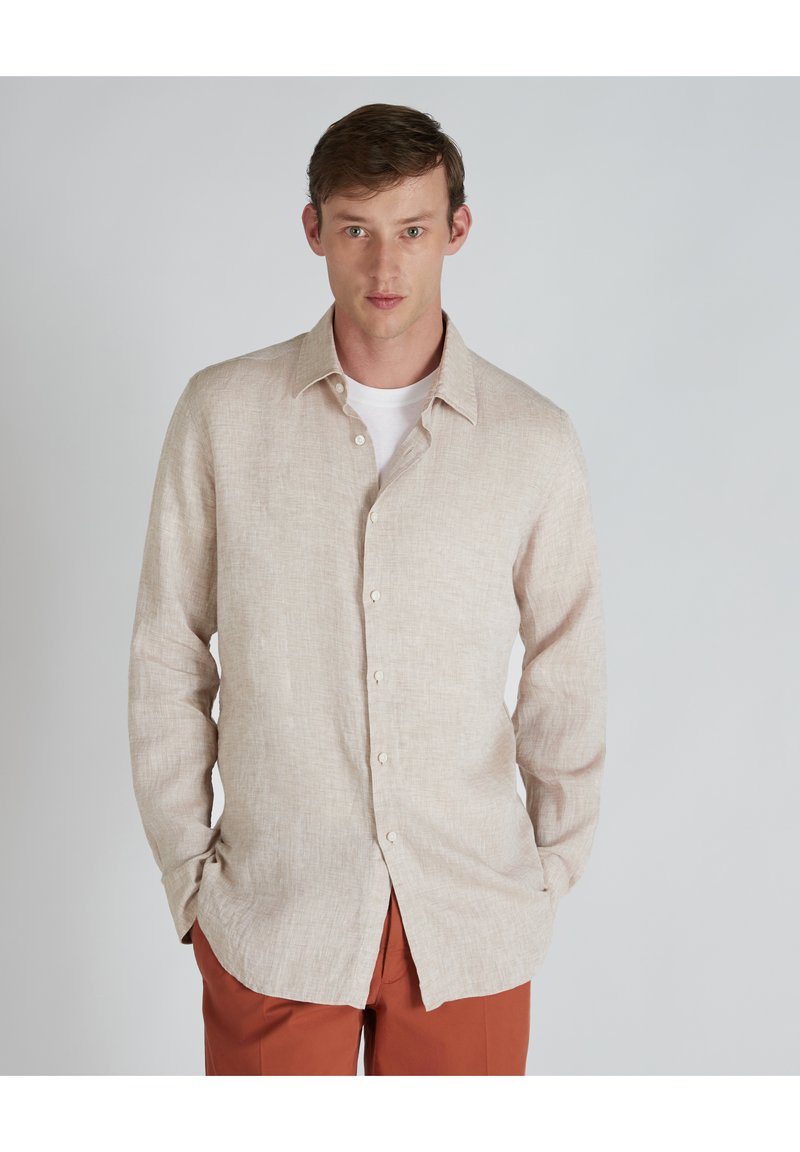 Camisa de lino beige claro con cuello puntiagudo, mangas largas y cierre frontal de botones; llevada sobre una camiseta blanca. Tejido suave y texturizado.