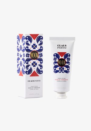 Crème pour les mains dans un tube blanc avec un motif floral bleu et un texte noir. Accompagnée d'une boîte décorative à motifs bleus, rouges et blancs.