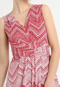 Robe à motif rouge et blanc avec un design enveloppant, décolleté en V et taille froncée. Présente des rayures géométriques et une légère texture.