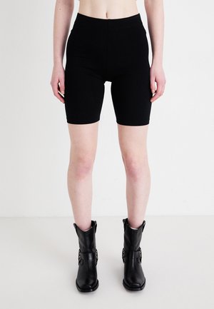 Black, stretchy bicycle shorts with a high waist, reaching mid-thigh, paired with black ankle boots featuring buckle accents.