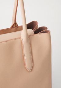 Borsa tote in pelle pesca con due manici corti e un design liscio e strutturato. Presenta ritagli nella parte superiore e cuciture visibili lungo i bordi.