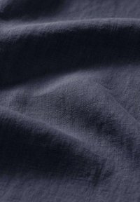 Tessuto blu scuro con una superficie liscia e strutturata, caratterizzato da un delicato motivo a trama. Sono visibili morbidi drappeggi e pieghe leggere.