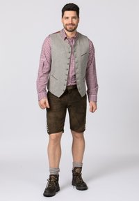 Grijze vest met knopen, rood geruit shirt, bruinleren shorts en donkere laarzen met grijze sokken. Kenmerken zijn contrasterende zakaccenten.