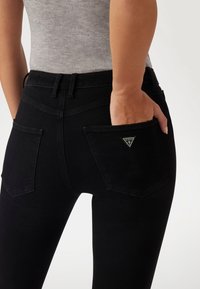 Black denim jeans with a fitted shape, featuring a single round stitched pocket and a small triangle logo on the back.