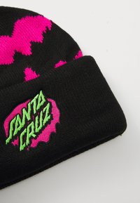 Bonnet en tricot noir présentant des taches roses vif et un logo "Santa Cruz" brodé en vert sur un fond rose.