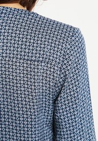 Gros plan d'une personne portant une chemise à manches longues bleu marine avec un petit motif circulaire en blanc et bleu clair.