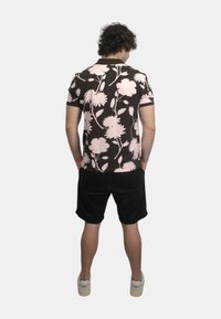 Camicetta a maniche corte con motivi floreali rosa e bianchi su uno sfondo marrone, abbinata a pantaloni corti neri e calzature leggere.