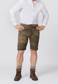 Shorts en cuir marron avec une finition texturée, dotés de boutons latéraux décoratifs et d'une ceinture ornée. Associés à une chemise blanche à col.
