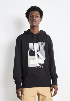 Sudadera negra con un diseño gráfico en blanco y gris, capucha con cordón y puños acanalados. Tejido suave con un corte relajado.