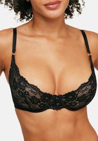 Soutien-gorge en dentelle noire avec armatures, doté de motifs floraux, de bretelles ajustables et d'accents en or au niveau des attaches des bretelles.