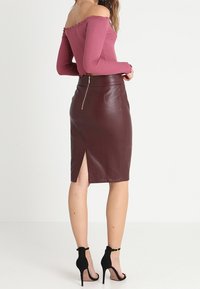 Burgundy pencil skirt with a back slit and metal zipper, paired with a fitted mauve off-shoulder top, featuring ruffled neckline.