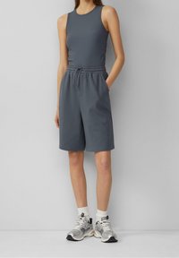 Grijs mouwloos geribd topje en bijpassende shorts met elastische taille en zakken, gecombineerd met zilveren sneakers en witte sportsokken.