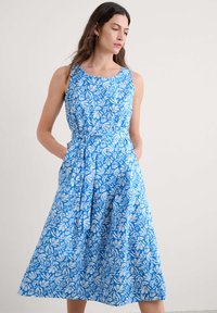 Rochie fără mâneci, de culoare albastră, cu un model alb în formă de frunză, având talie ajustată și fustă vaporoasă. Fabricată din material ușor, include buzunare laterale.
