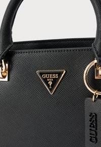 Must tekstureeritud käekott kuldse tooniga riistvaraga. Omab kolmnurga kujulist logo ja sildi, millel on reljeefne brändinimi. Tugevad topeltkäepidemed.